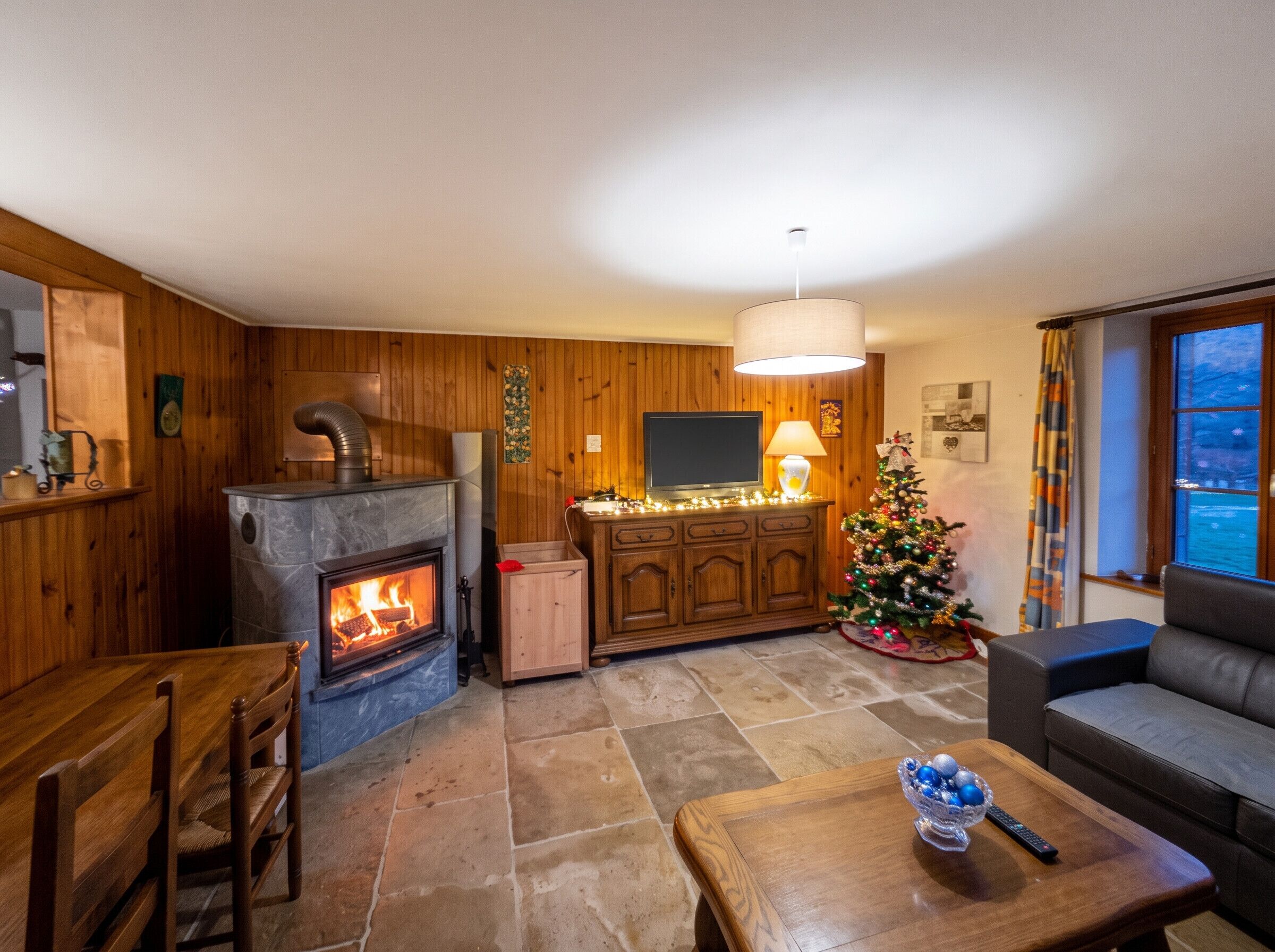 A cozy living room with a fireplace, a television, a Christmas tree, and a sofa.