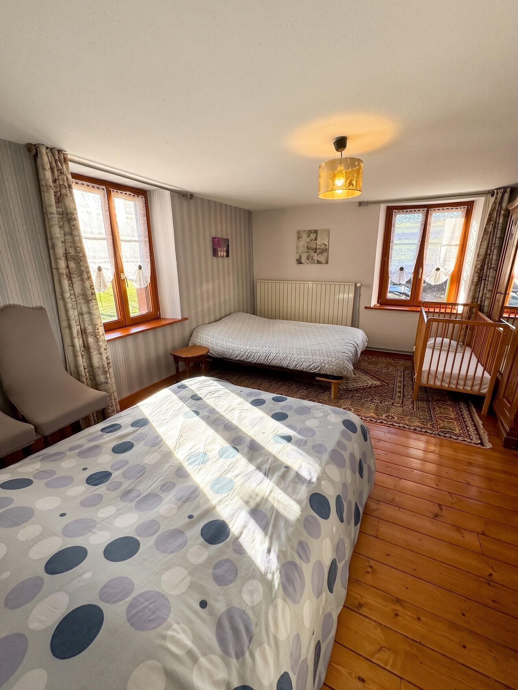 A bedroom with a bed, a chair, a crib, and a window.