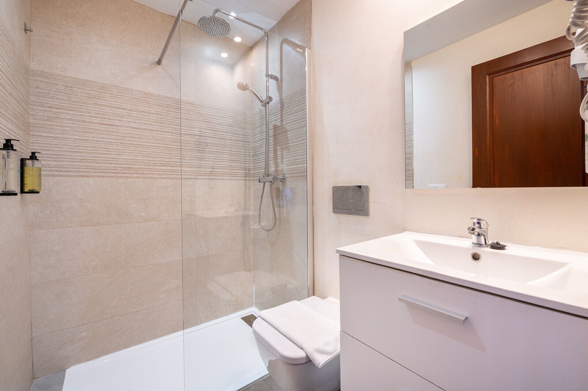 Un baño moderno con ducha envuelta en cristal, lavabo blanco y puerta de madera.
