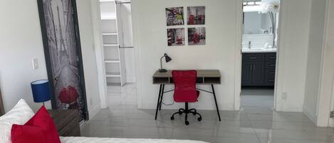 Un dormitorio con cama, escritorio, silla y baño a la vista a través de una puerta abierta.