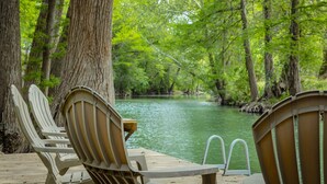Une terrasse en bois, agrémentée de chaises Adirondack, donnant sur une rivière paisible bordée d’arbres.