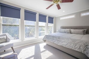 A bedroom with a large bed, a ceiling fan, and multiple windows with blue blinds.