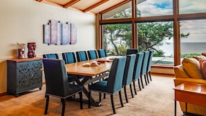 Un espace repas comprenant une grande table et des chaises, un meuble décoratif et une vue sur la mer grâce à de grandes fenêtres.