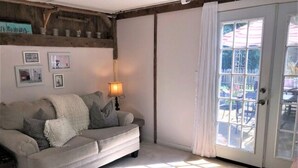A living room with a sofa, a lamp, and a view through a glass door to an outdoor area. - The Parson’s Cottage (Orleans)