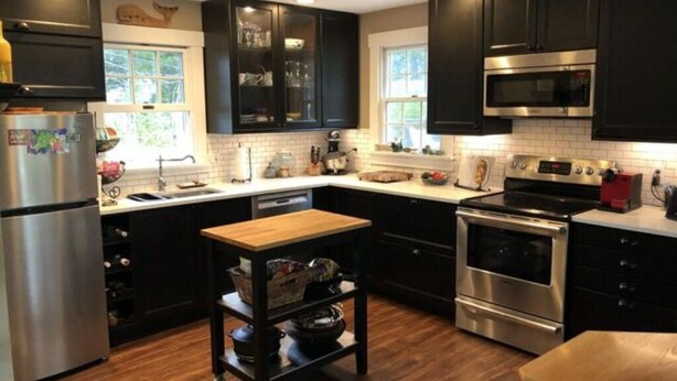 A modern kitchen with dark cabinets, stainless steel appliances, and a wooden island. - The Parson’s Cottage (Orleans)