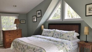 A bedroom with a bed, a dresser, a nightstand, and a window. - The Parson’s Cottage (Orleans)