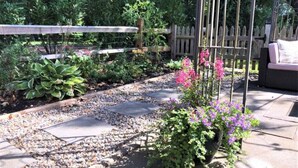 A garden pathway with stepping stones, surrounded by various plants and a wooden fence. - The Parson’s Cottage (Orleans)
