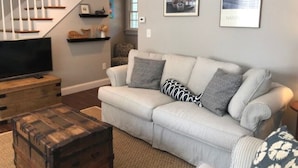 A living room with a sofa, a wooden chest, and a television. - The Parson’s Cottage (Orleans)