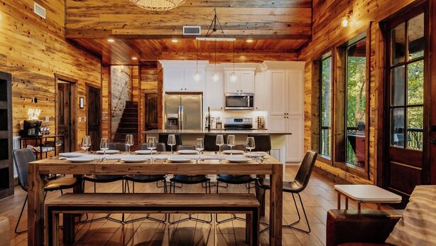 L’intérieur d’un chalet en bois comprend un coin repas, une cuisine et de grandes fenêtres.