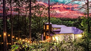 Une maison moderne entourée d’arbres, illuminée de guirlandes lumineuses.