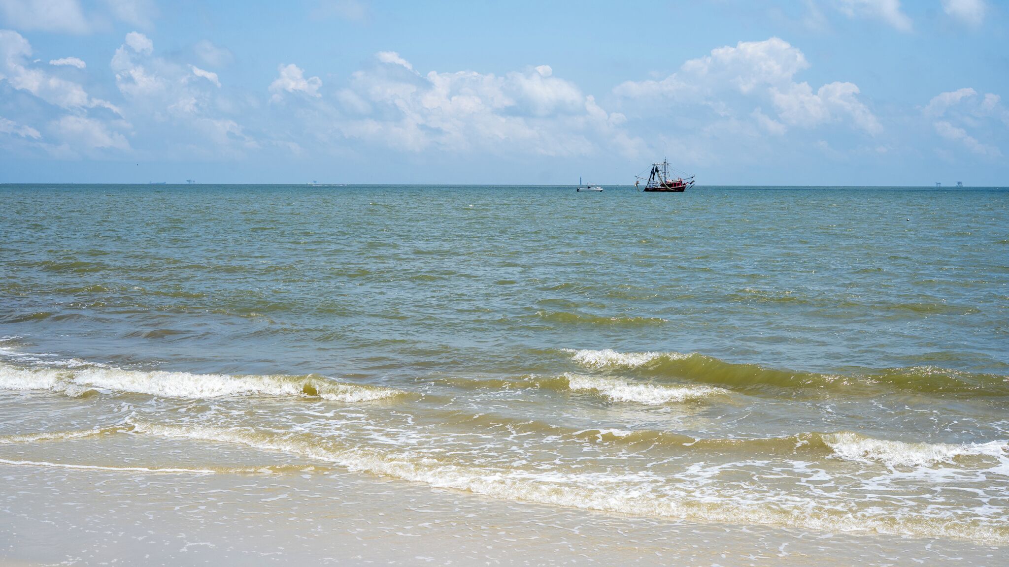 Ein Strand mit sanften Wellen und einem entfernten Boot.