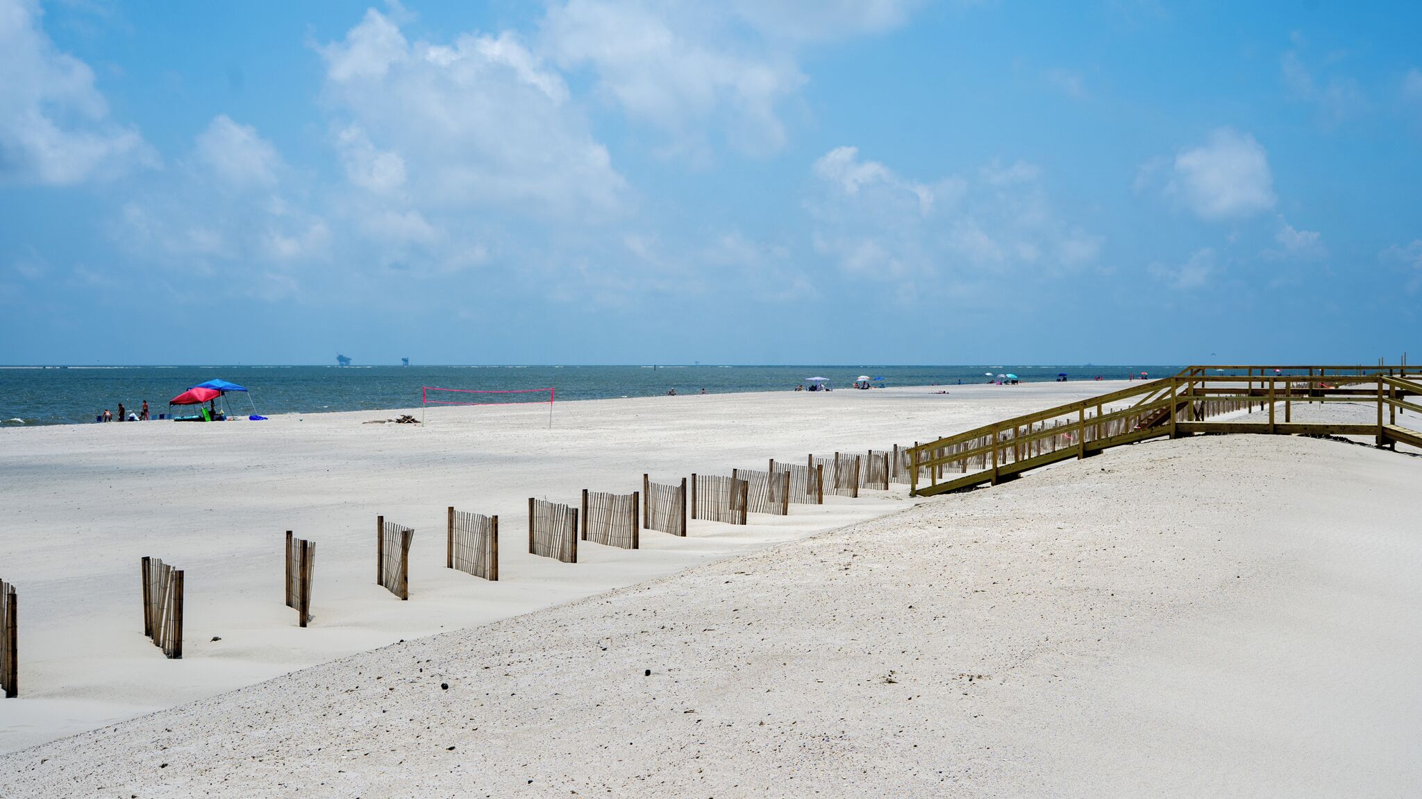 Une plage de sable avec une promenade en bois et un filet de volley-ball.