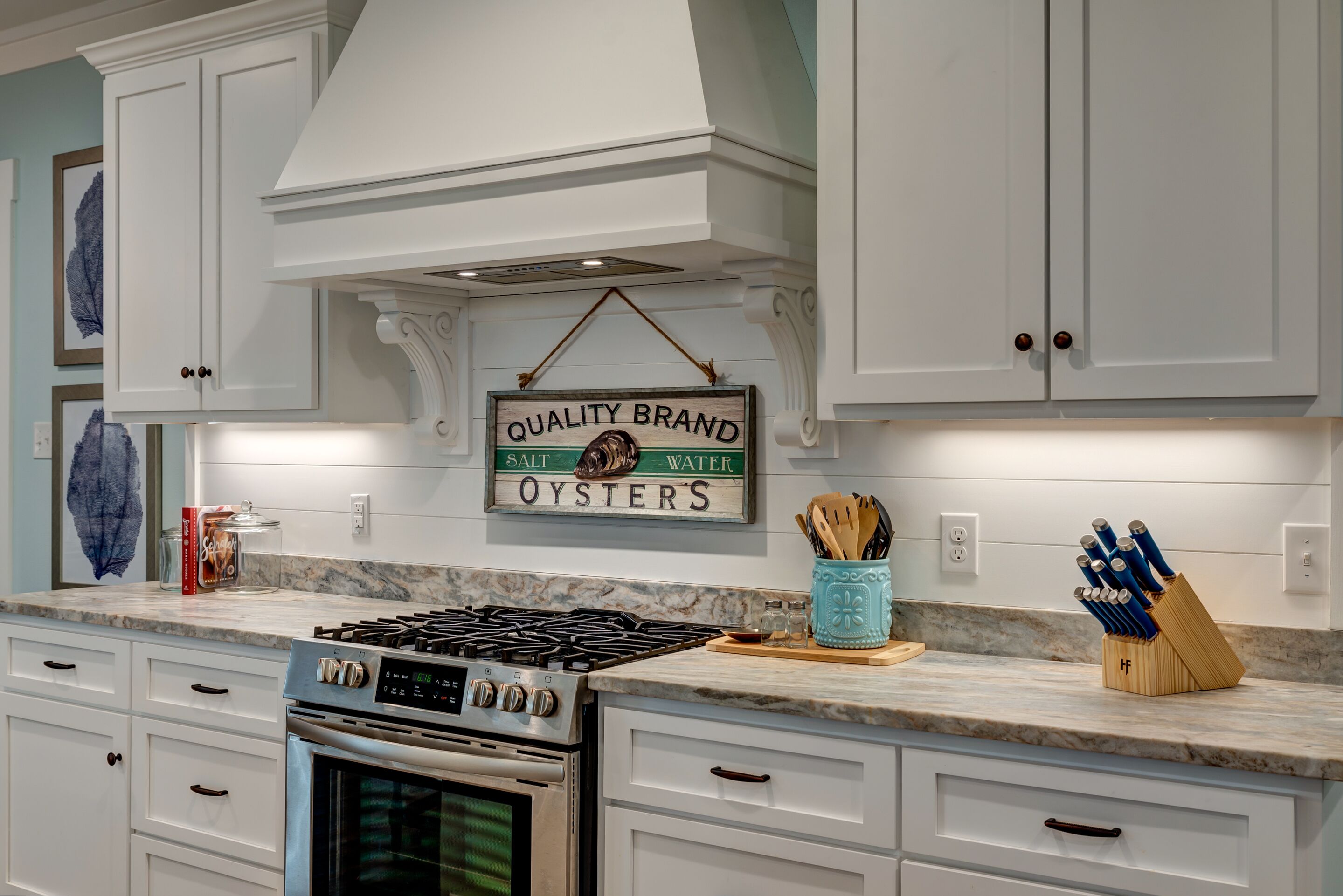 A kitchen with white cabinetry, a gas stove, and a sign that reads "QUALITY BRAND SALT WATER OYSTERS."