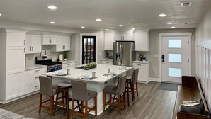 A modern kitchen with white cabinetry, a large island with bar stools, a stainless steel refrigerator, and recessed ceiling lights. - Location, comfort and cleanliness.<br>Whole basement 1600-plus square feet.  (LEHI CITY)
