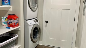 A laundry room with two stacked front-loading washers, a white door, and shelves with cleaning supplies. - Location, comfort and cleanliness.<br>Whole basement 1600-plus square feet.  (LEHI CITY)