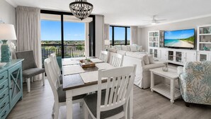 Amplia sala de estar con mesa de comedor, muebles blancos, televisor y vistas al exterior.