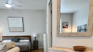 Een slaapkamer met een bed, nachtkastje, kapstok, spiegel en plafondventilator.