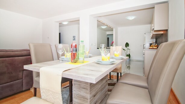 A dining area with a wooden table, beige chairs, and a white table runner. There are bottles and glasses on the table. - ESMA 2 - Deluxe Apartment (Rovinj)