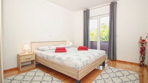 A bedroom with a wooden bed, two bedside tables with lamps, a window with curtains, and a view of greenery outside. - ESMA 2 - Deluxe Apartment (Rovinj)