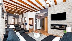 Ein modernes Wohnzimmer mit Kamin, Flachbildfernseher und Essbereich, im Hintergrund eine Küche.