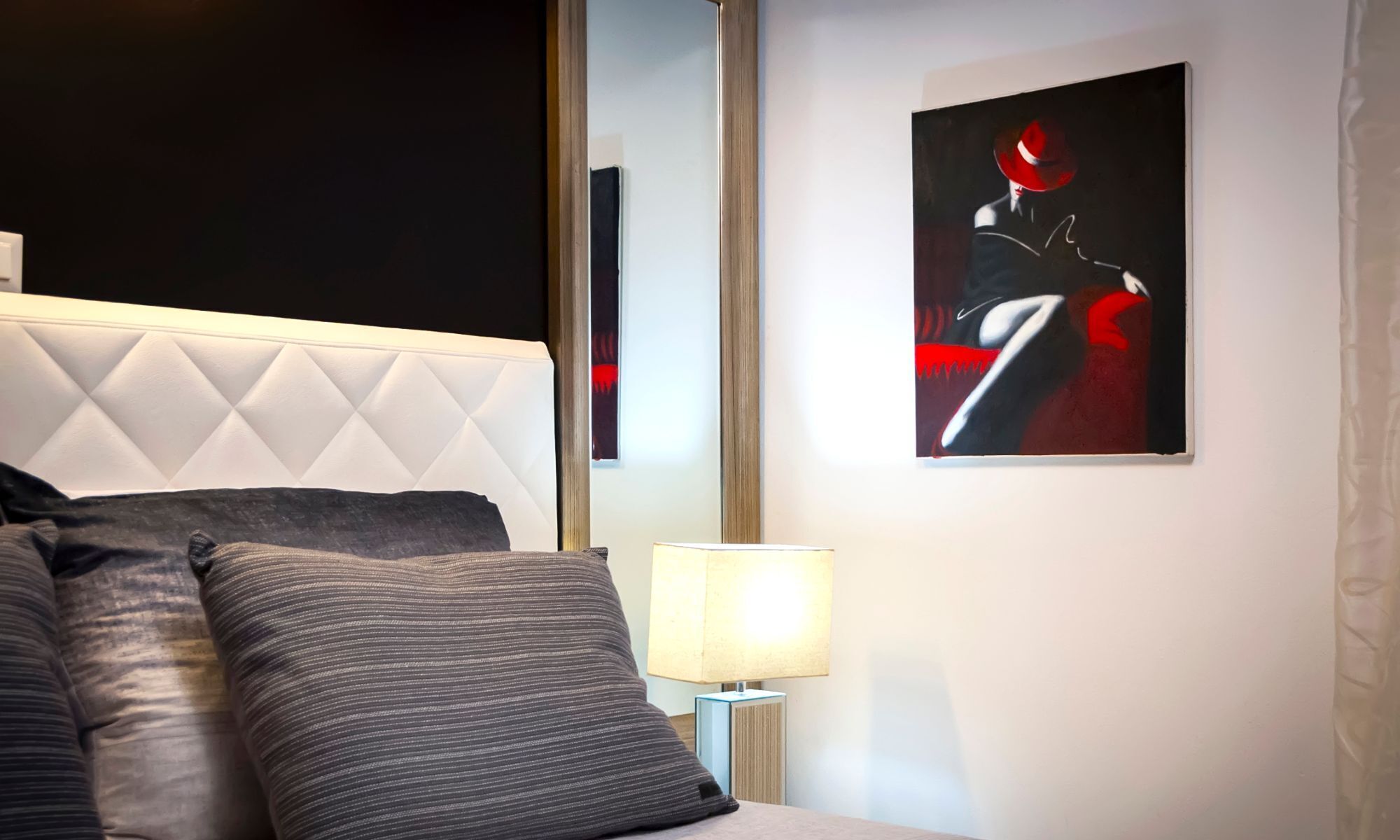 Une chambre à coucher moderne avec une tête de lit capitonnée, une lampe de chevet et un tableau abstrait encadré.