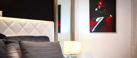 Une chambre à coucher moderne avec une tête de lit capitonnée, une lampe de chevet et un tableau abstrait encadré.