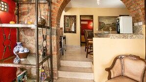 A cozy interior with a brick archway leading to a dining area, a kitchen with a water dispenser, and a seating area with a sofa.