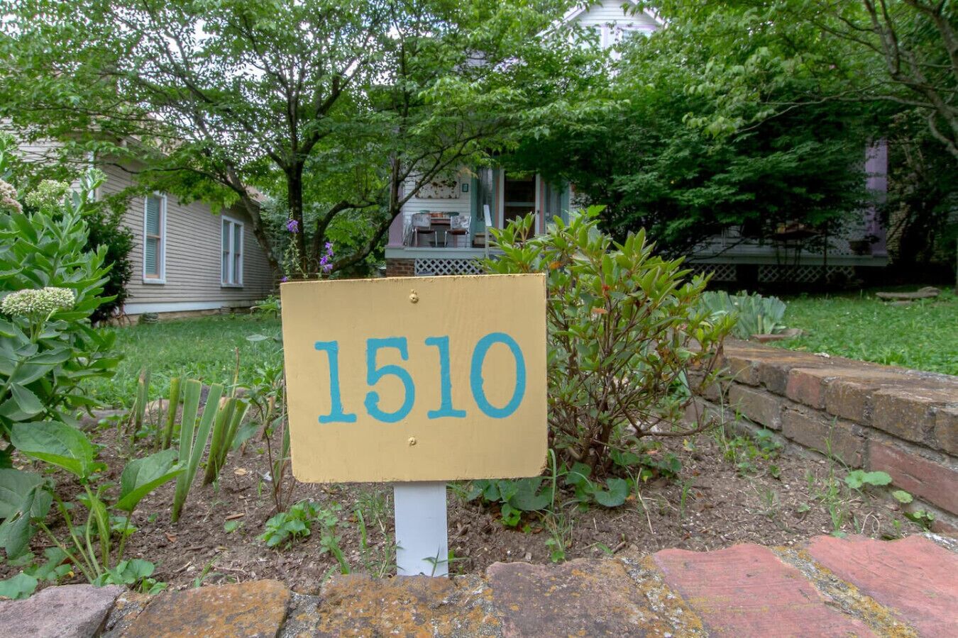 Une plaque indiquant le numéro de la maison, placée dans un jardin, avec un mur en briques et de la verdure tout autour.