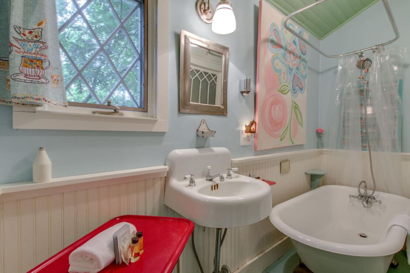 A bathroom with a white sink, a bathtub, and a window with a view of trees.