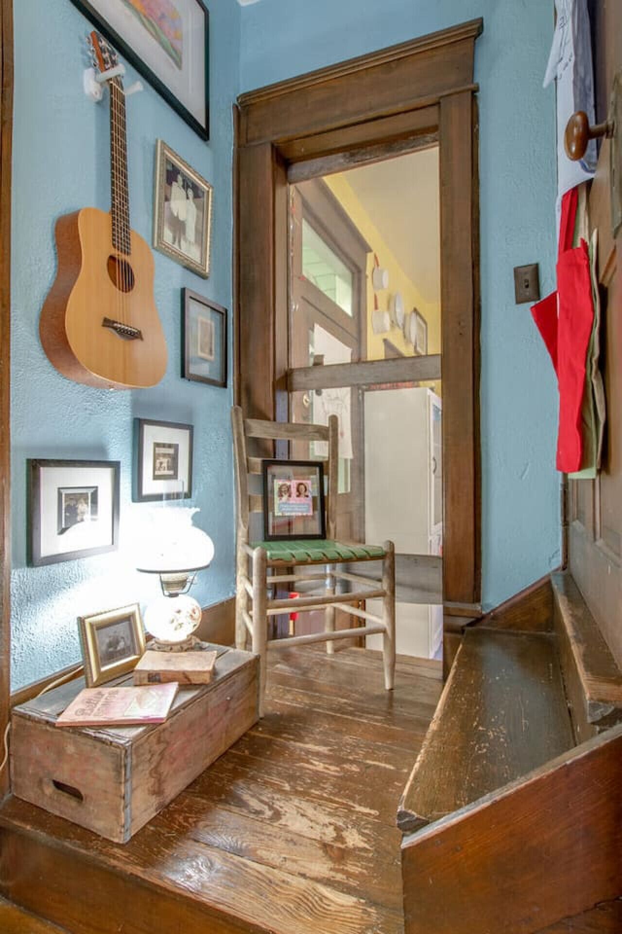 A room with a wooden staircase leading to a door, a guitar hanging on the wall, and framed pictures.