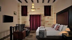 A hotel room with a bed, a desk, a chair, a TV, and a chandelier. - Grand Master Suite (Rodos)
