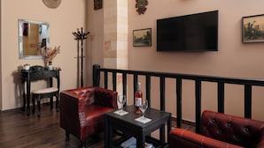 A room with a TV, a table with a bottle and glasses, a red sofa, a chair, and a small table with a vase. - Grand Master Suite (Rodos)