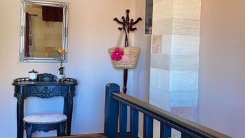 A hallway with a brown leather chair, a mirror, a small table with decorative items, a wall-mounted air conditioner, and a stone wall.