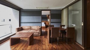 Una sala moderna con una mesa de centro de madera, un sofá y una mesa de comedor con sillas. La habitación tiene un ventanal con vistas a la ciudad.