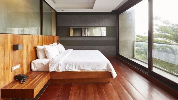 Un dormitorio moderno con una cama grande, paneles de madera, televisión integrada y un ventanal con vistas a zonas verdes.