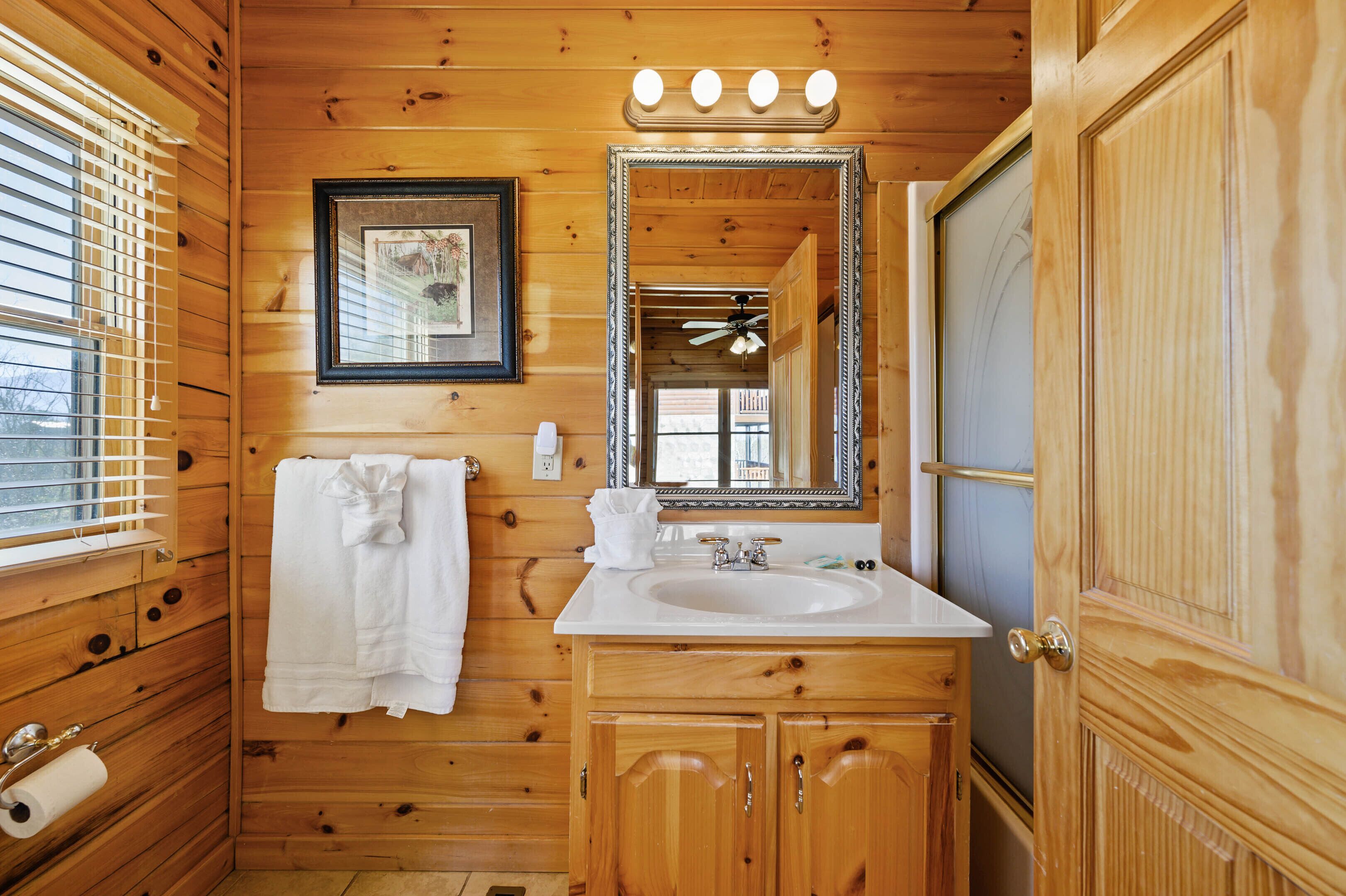 A wooden cabin bathroom with a sink, mirror, towel rack, and a framed picture on the wall.