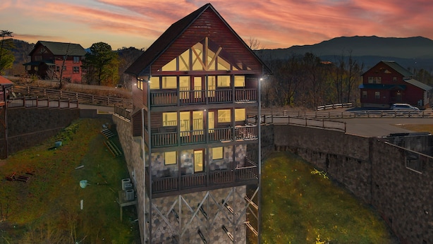 A multi-story building with a stone facade and a balcony, surrounded by a stone wall and a grassy area. - Specials! Stunning Views+Location. 4 King Beds w/ en suite. Hot Tub, Games! (Sevierville)