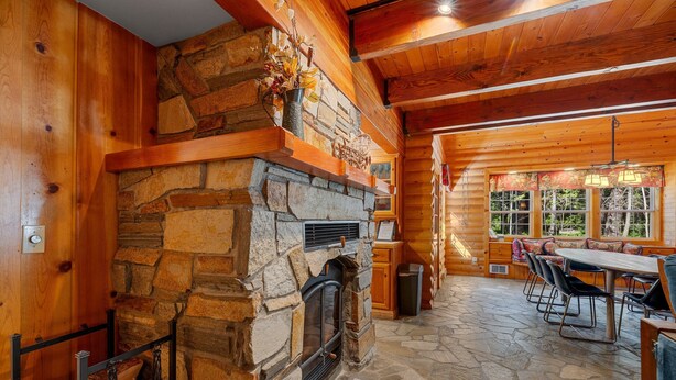 A log cabin interior with a stone fireplace, wooden walls, a stone floor, and a dining area with outdoor seating.