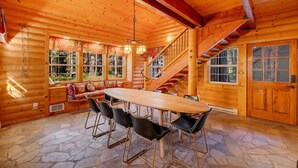 A log cabin with a stone floor, wooden dining table, black chairs, a staircase, and large windows.