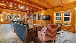 A log cabin interior with a stone floor, wooden furniture, a TV, and a staircase.