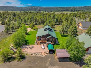 A lodge with a large deck, a fire pit, and a view of a forested area.