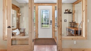 A wooden-framed entrance with a glass door, a bench, a small table with a basket, and a decorative horse figure.