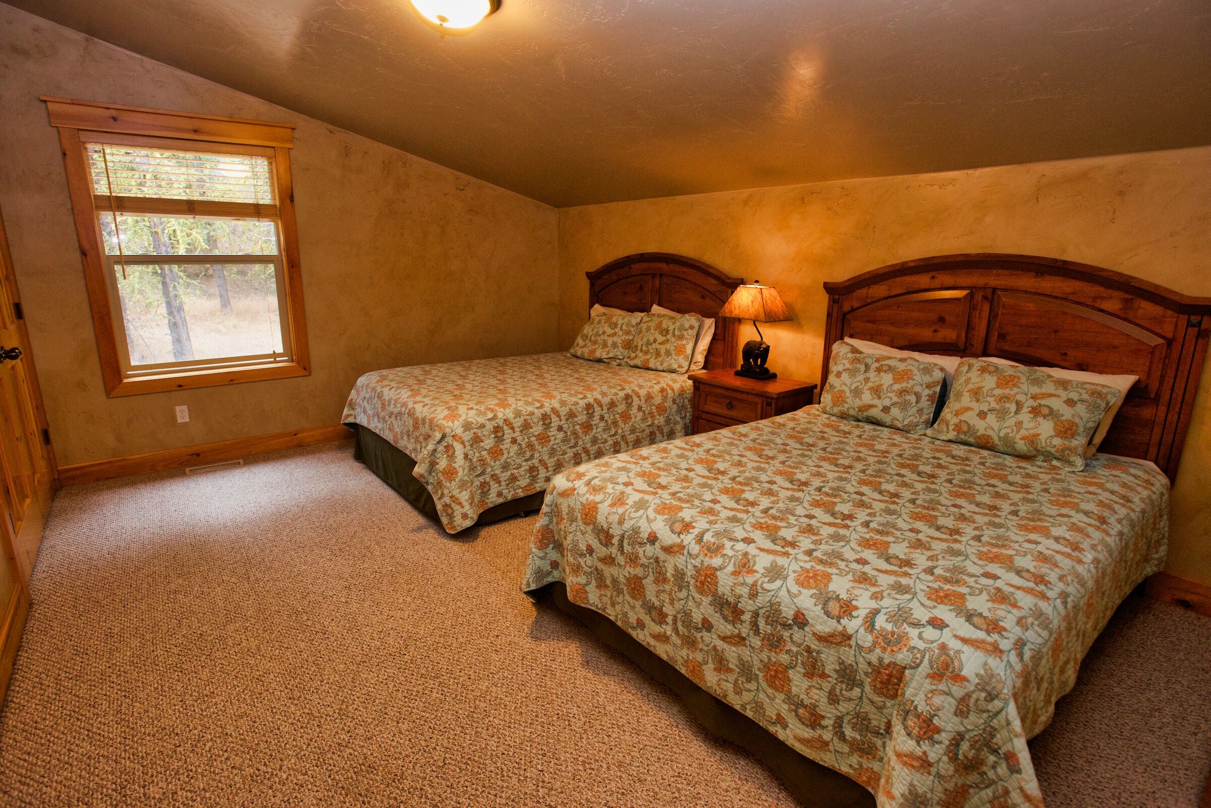 A bedroom with two beds, a window, and a lamp.