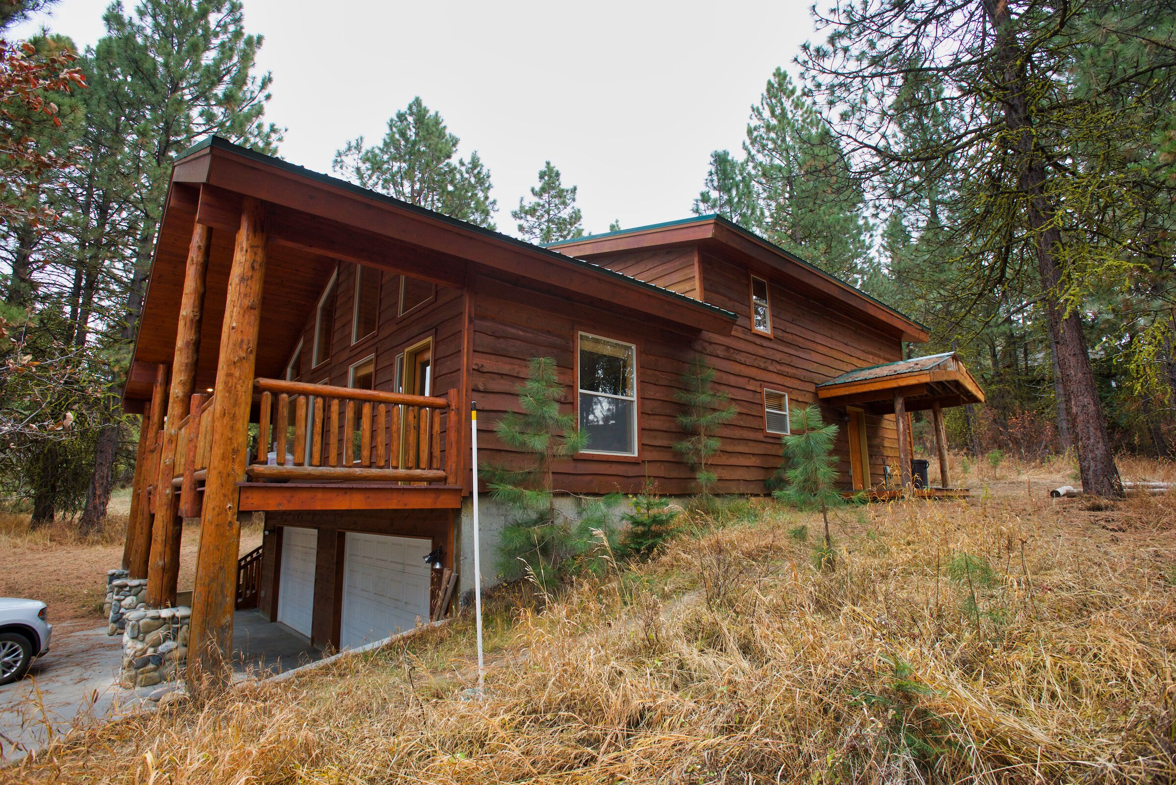 Une cabane en bois dotée d’une véranda, d’un garage et située dans un cadre naturel, au cœur d’une forêt.