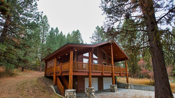 Une cabane dotée d’une terrasse en bois, de piliers en pierre et d’un porche abrité.