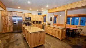 Una cocina amplia con armarios de madera, un refrigerador de acero inoxidable, una isla grande y una zona de comedor con mesa y sillas.