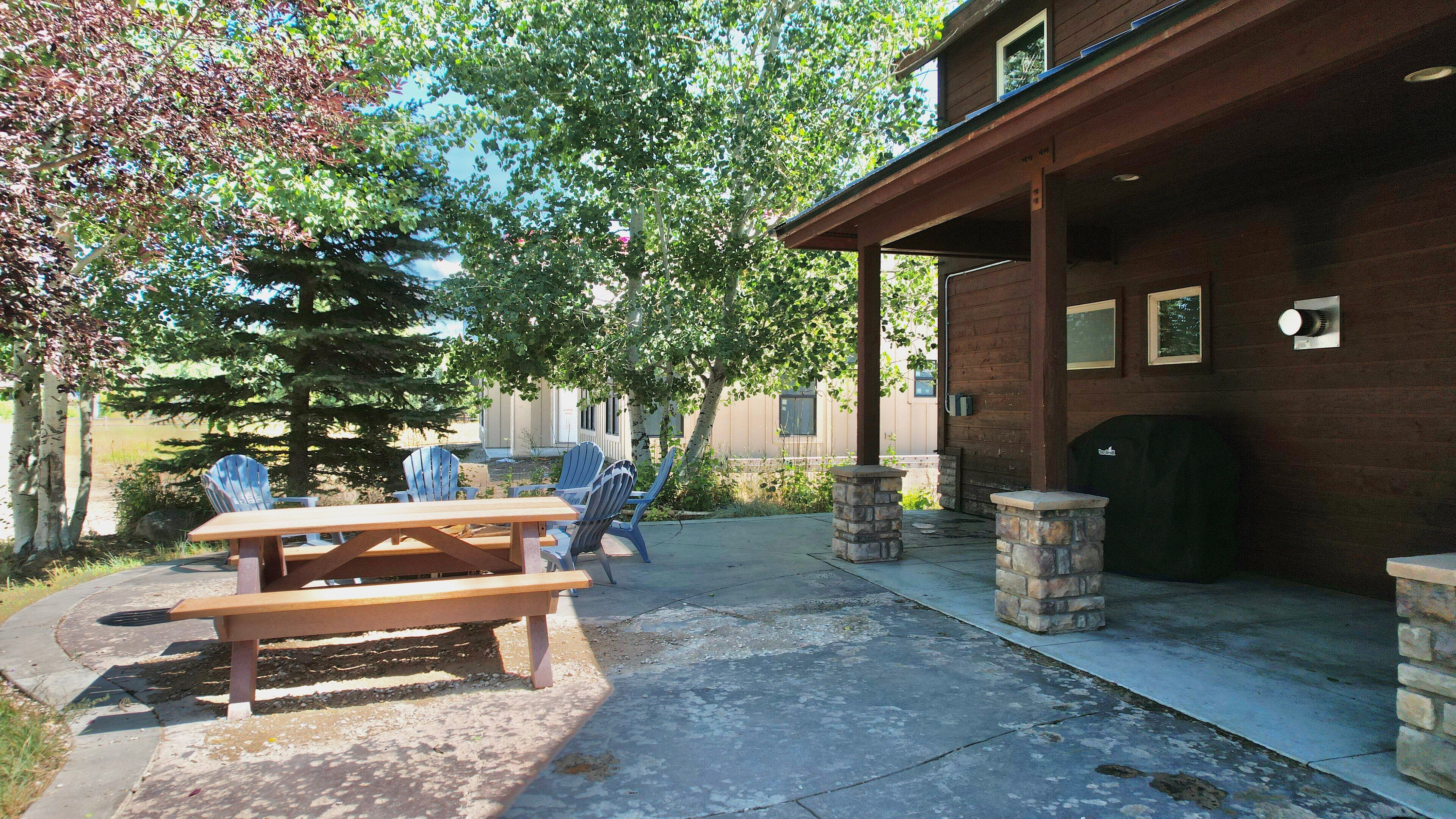 Un patio al aire libre con mesas y sillas de picnic, una chimenea de piedra y un edificio de madera con ventanas y una puerta.