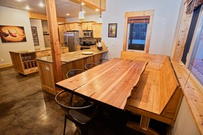 Une table à manger en bois avec des chaises, un coin cuisine avec des meubles en bois et une fenêtre donnant sur un beau paysage.