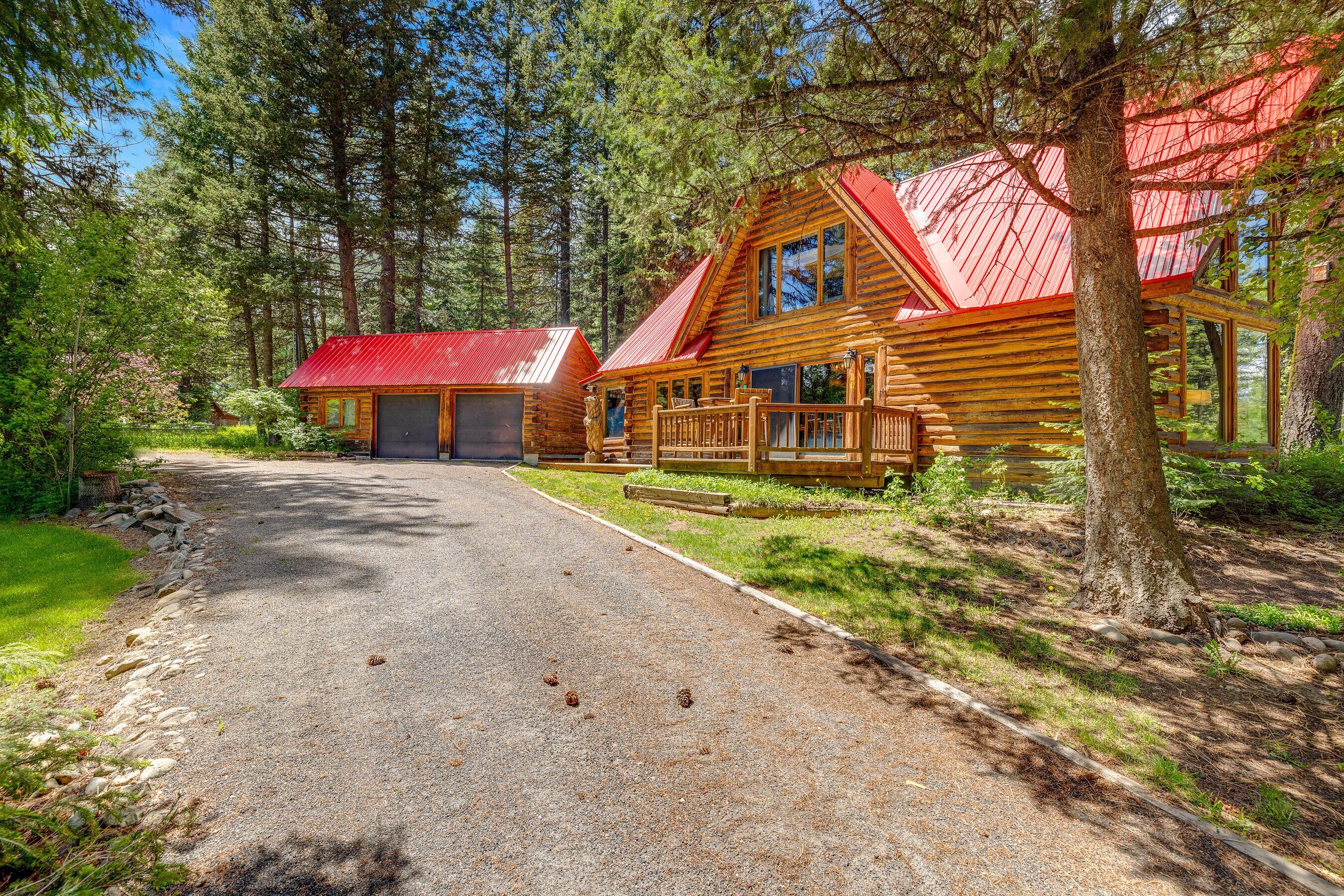A log cabin with a red roof, surrounded by a forest.