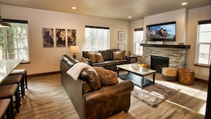 A modern living room with a leather sofa, a coffee table, a fireplace, and a flat-screen TV mounted above it. - Suite Retreat: Short Walk to Downtown McCall, A/C, Propane Fireplace (McCall)